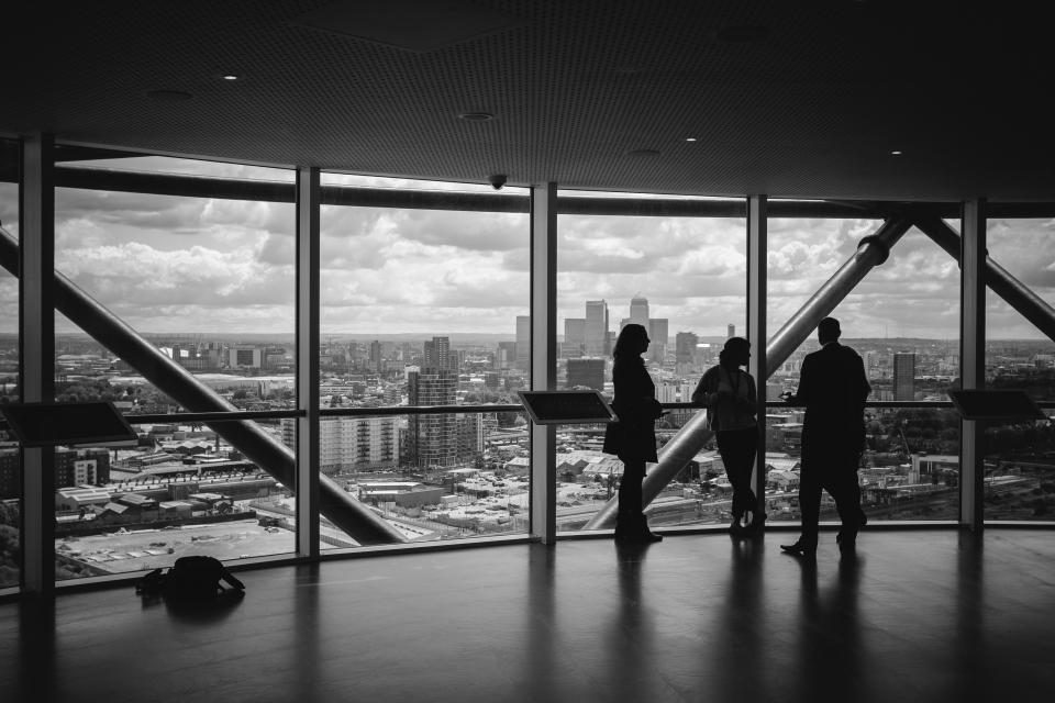 Trois personnes dans un bureau vitré qui domine la ville, en noir et blanc