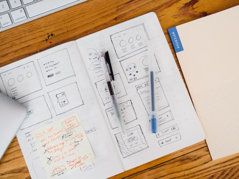 Un carnet ouvert sur un bureau en bois, couvert de croquis d'écrans et de notes