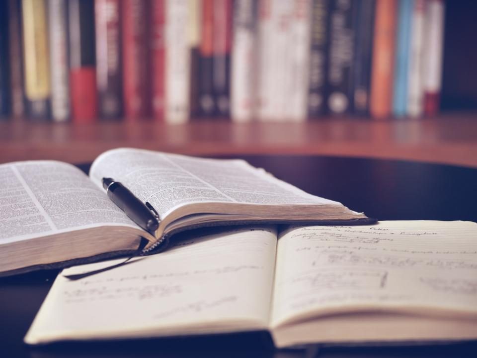 Un livre ouvert et un cahier annoté posés sur une table, un stylo entre les pages