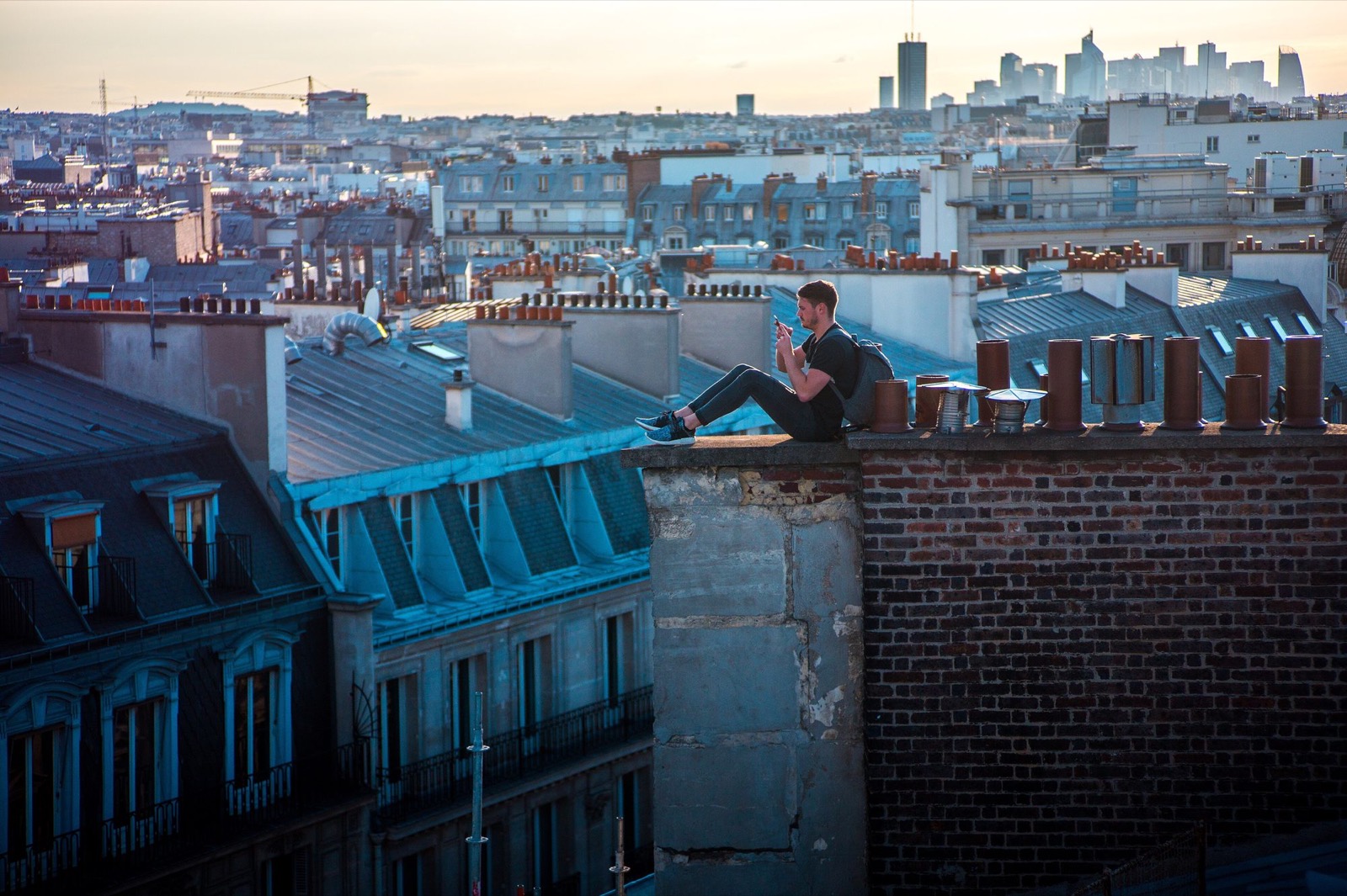 Un homme assis sur un toit de Paris, téléphone à la main