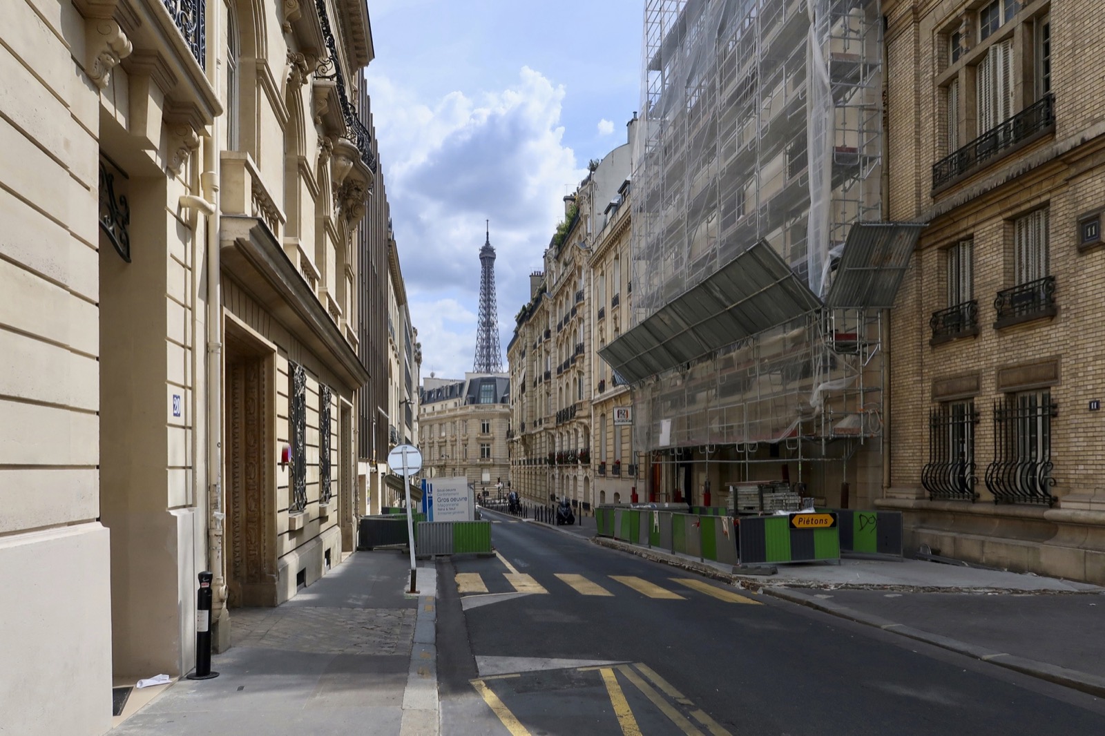 Une rue du 16e arrondissement de Paris : un immeuble haussmannien en rénovation sous échafaudage, la tour Eiffel au loin